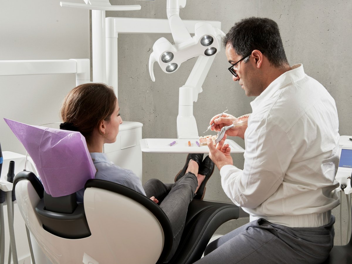 Dentist explaining treatment with a dental model to a patient seated in a treatment chair