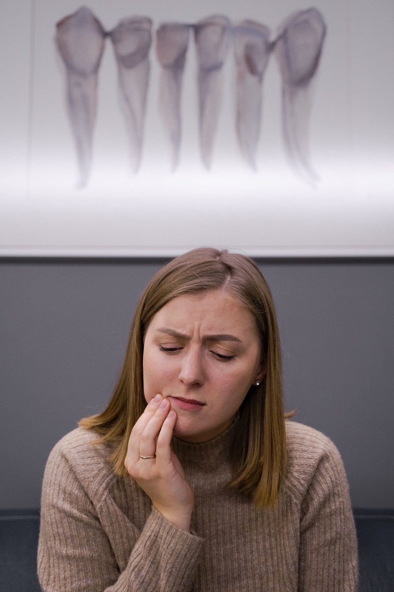 A woman holding her jaw in discomfort in front of a dental X-ray of lower teeth